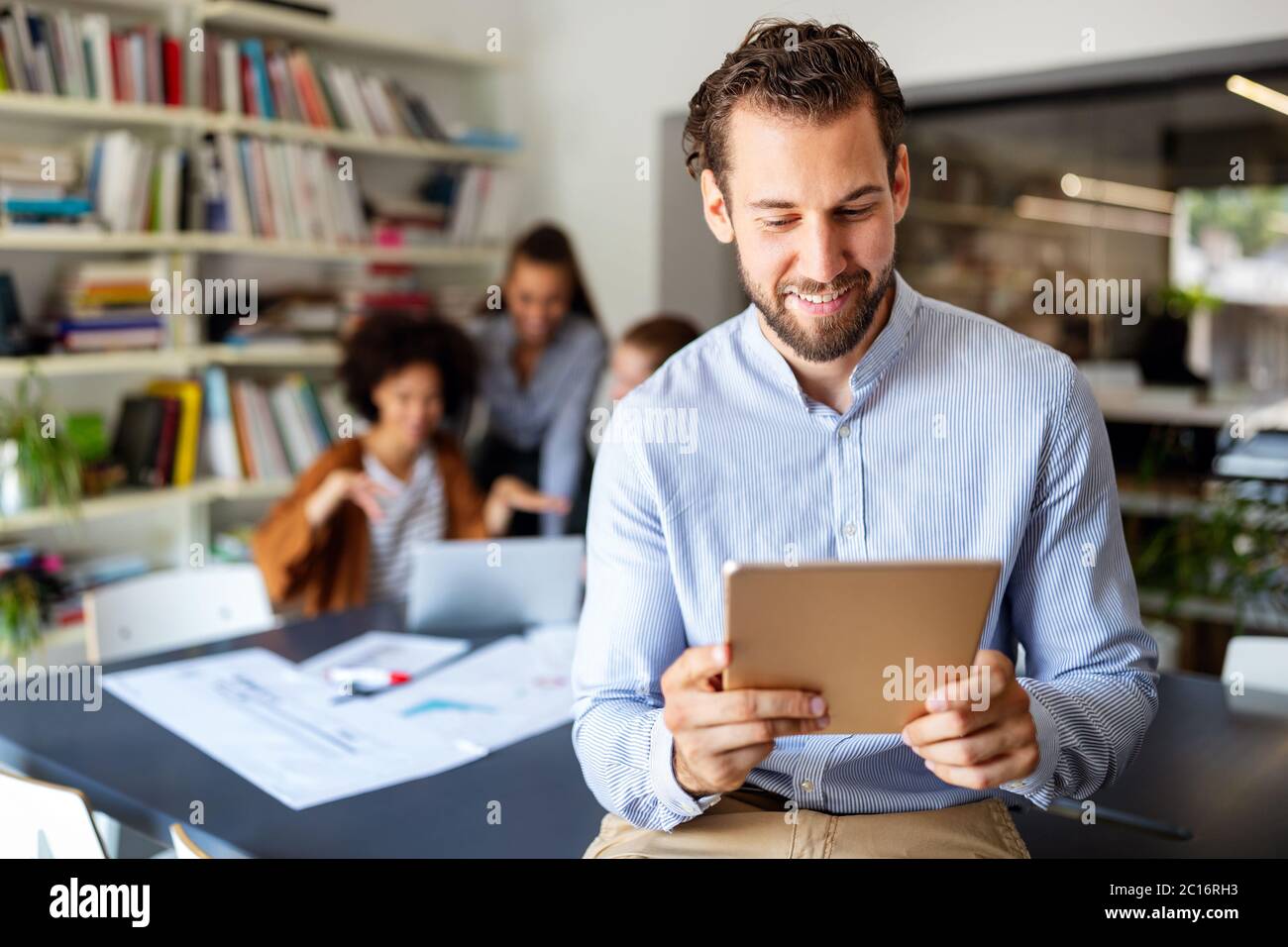 Smiling designer using his tablet pc while team works behind Stock Photo