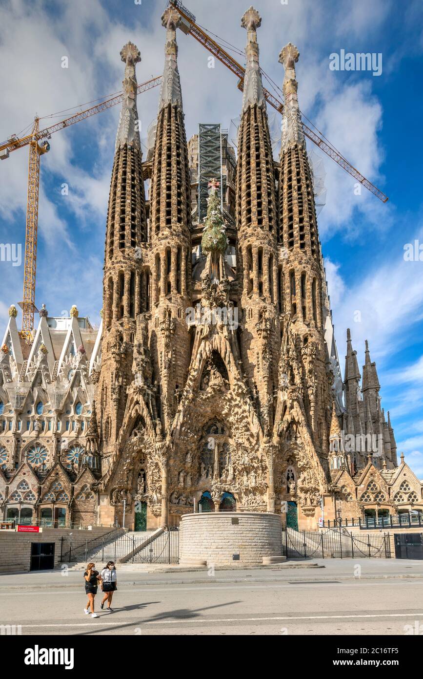 Two girls wearing surgical mask walking in front of the Sagrada Familia basilica closed to visitors due to the covid-19 pandemic, Barcelona, Spain Stock Photo