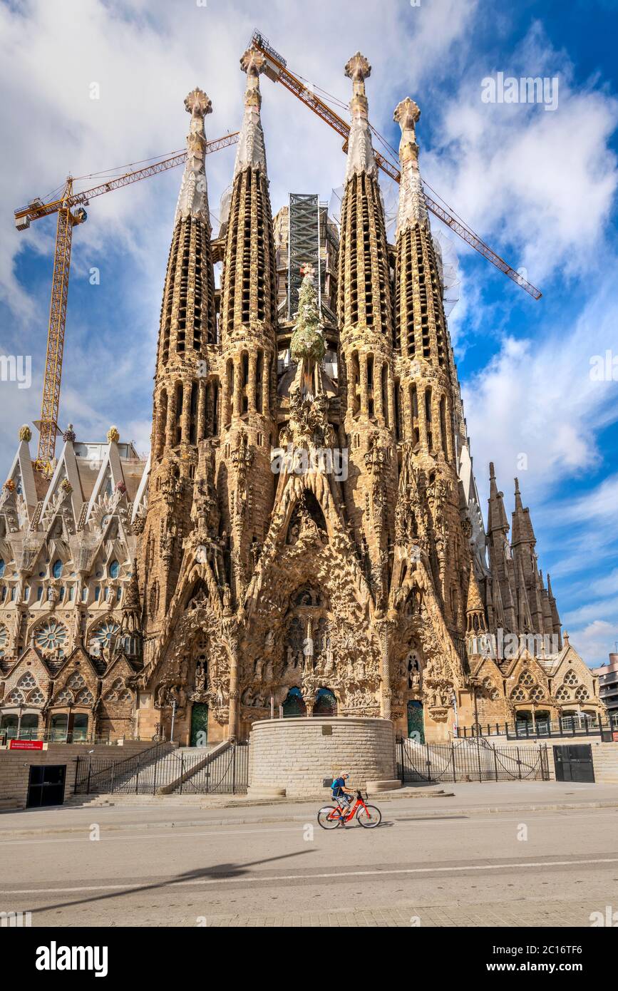 Man wearing surgical mask riding a bike in front of the Sagrada Familia basilica church closed to visitors due to the covid-19 pandemic, Barcelona Stock Photo
