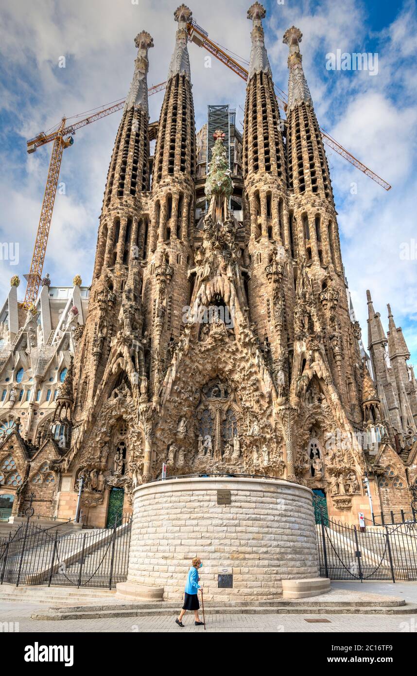 Old woman wearing surgical mask walking in front of the Sagrada Familia basilica closed to visitors due to the covid-19 pandemic, Barcelona, Spain Stock Photo