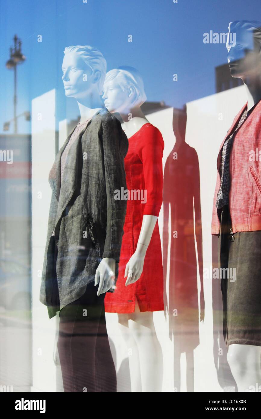 Shadow of a woman's mannequin in a red dress, a man and a woman in trendy suits in a shop window. Stock Photo