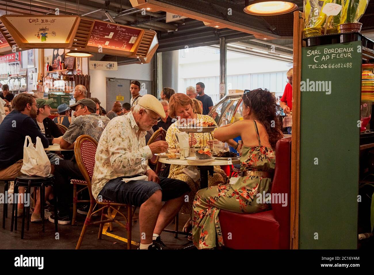 Groups of people sit at tables enjoying shellfish and seafood platters at chez  jean mi Capuchin Market (Marche des capucins) Bordeaux France Stock Photo -  Alamy