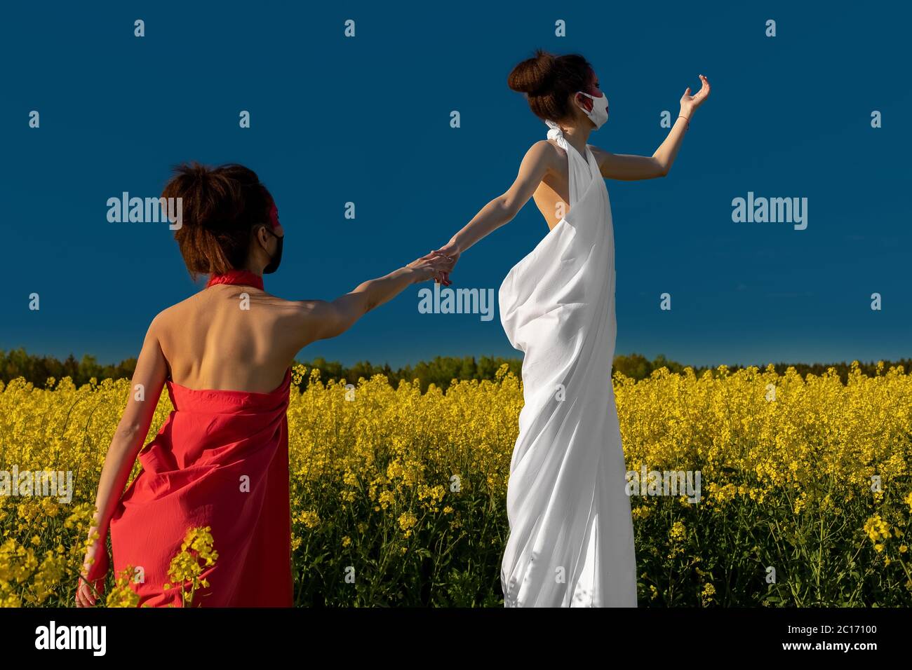 Two beautiful young brunette girls with creative bright makeup in tunics on a background of a field of yellow flowers and a blue sky. Two girls in med Stock Photo