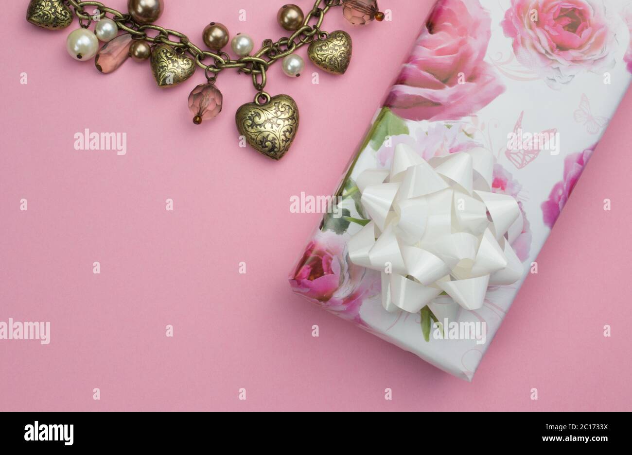 Background with gold heart and pearl necklace, wrapped rose gift wrapped present isolated on pink Stock Photo