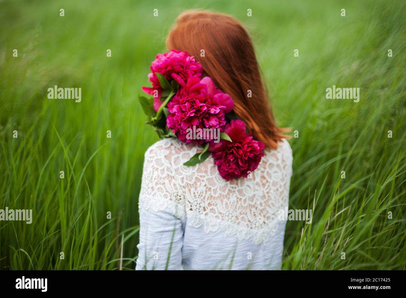 Girl with peony bouquet sitting in the grass Stock Photo