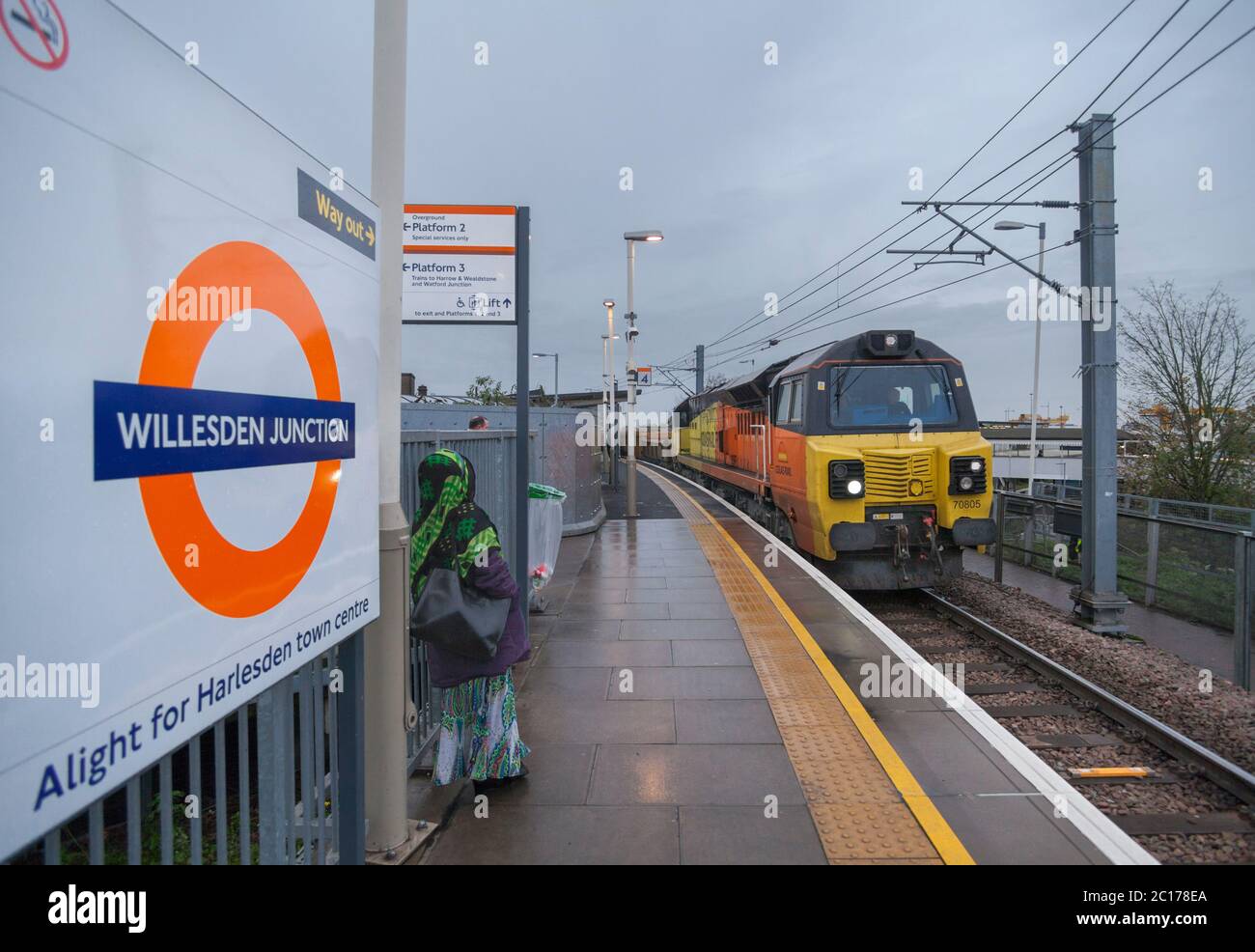 Colas rail Freight class 70 locomotive 70805 passing the London Overground roundel logo at Willesden Junction High level railway station. Stock Photo