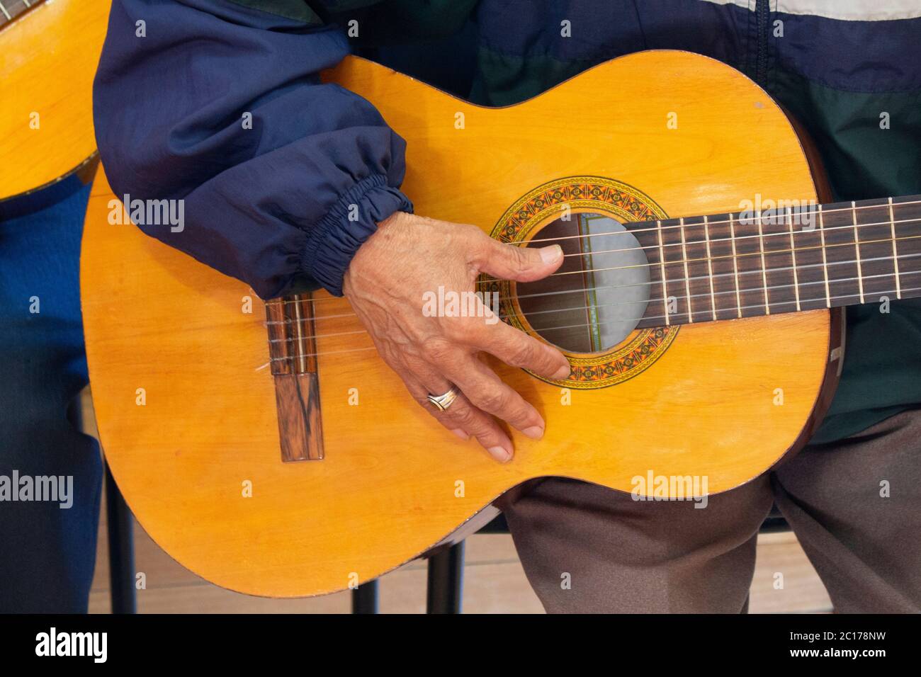 Approach to the hand of an elderly man sitting holding a guitar dressed in a blue shirt with a ring on his finger Stock Photo
