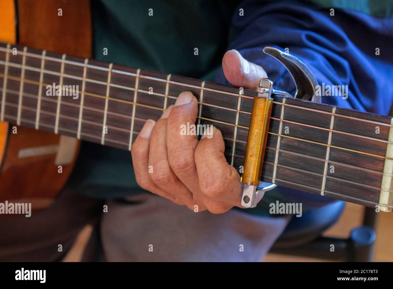 Approach to the left hand of an elderly man sitting playing a guitar dressed in a blue shirt Stock Photo