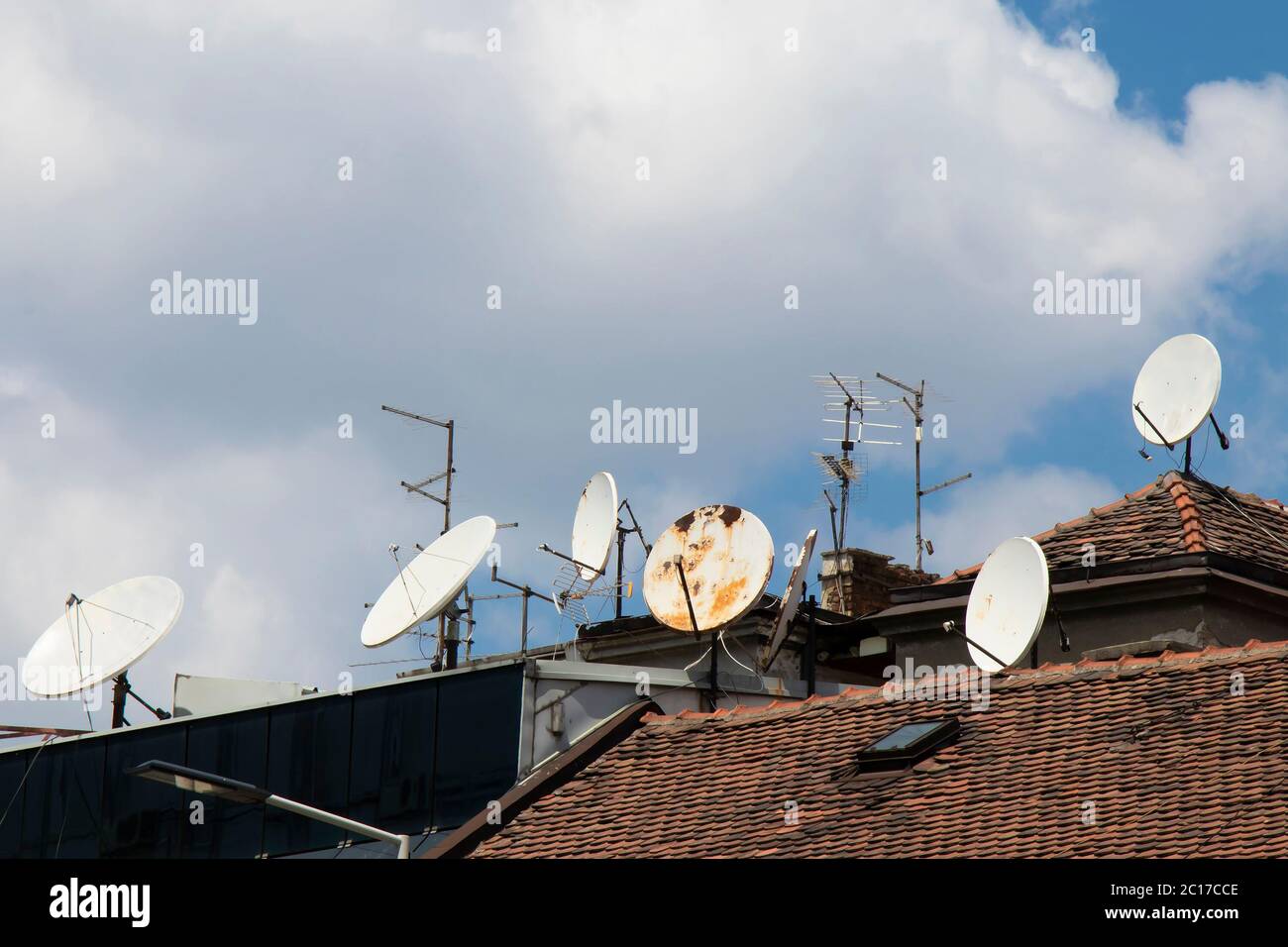 Satellite dishes and tv antennas mounted on roof tops against the sunny cloudy sky Stock Photo