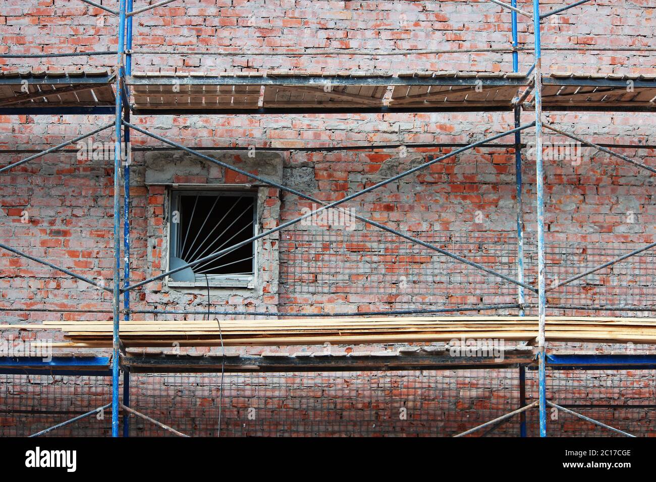 Blue scaffolding on an old brick house at the time of finishing and plastering work. Window with a lattice. Restoration work. Stock Photo