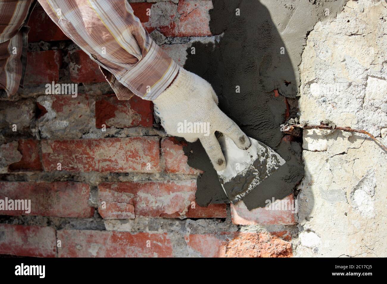 A professional builder bricklayer with hand trowel applies cement mortar to the brick wall in front of the lining during the res Stock Photo