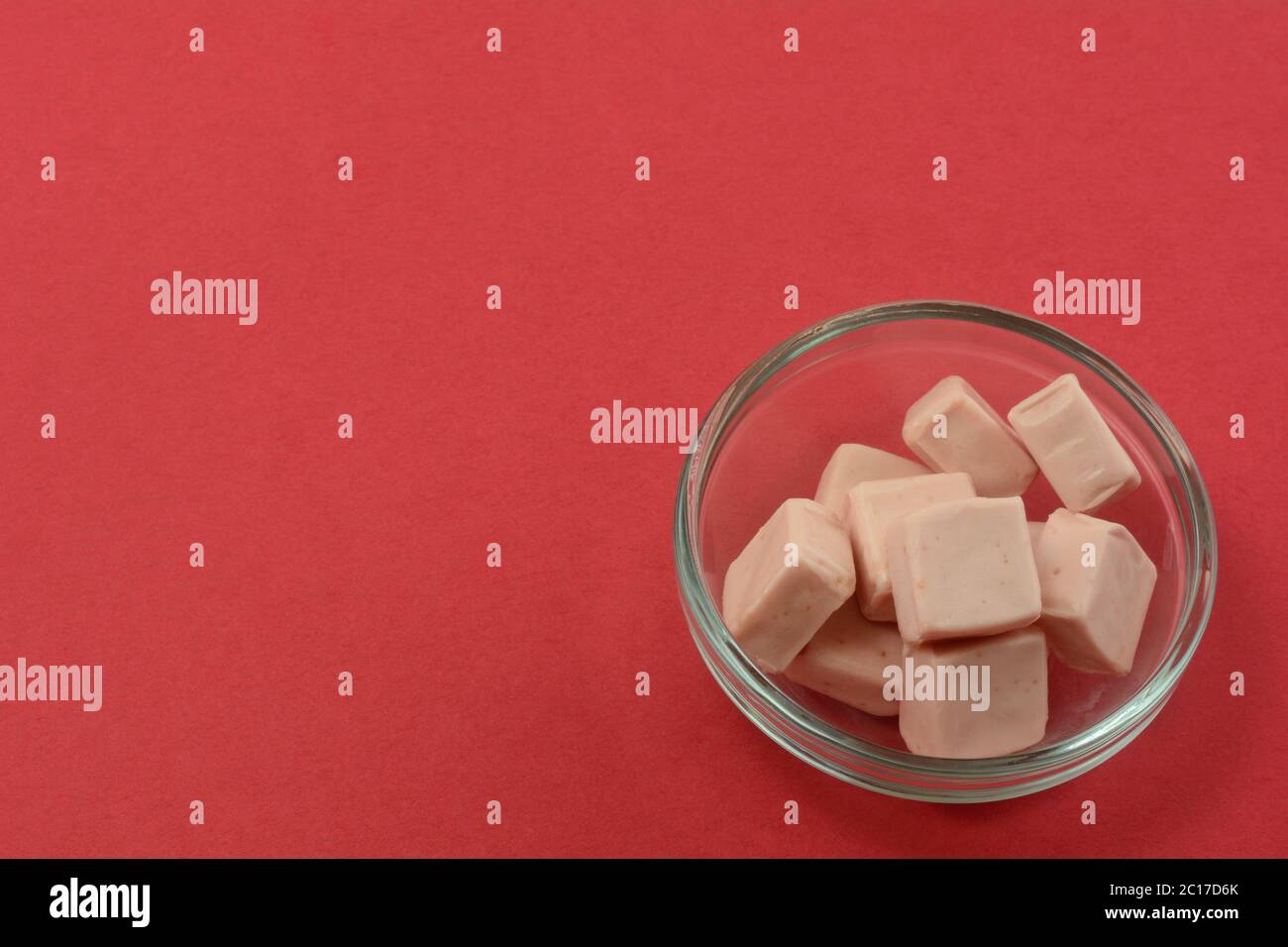 Strawberry toffee candy squares in glass candy bowl on red background Stock Photo