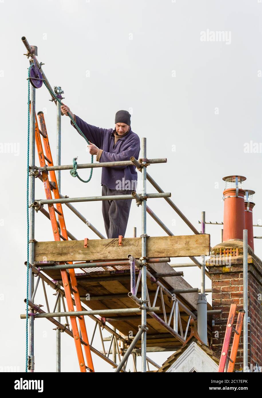 Construction worker on scaffolding tower over a roof during house repair in UK Stock Photo