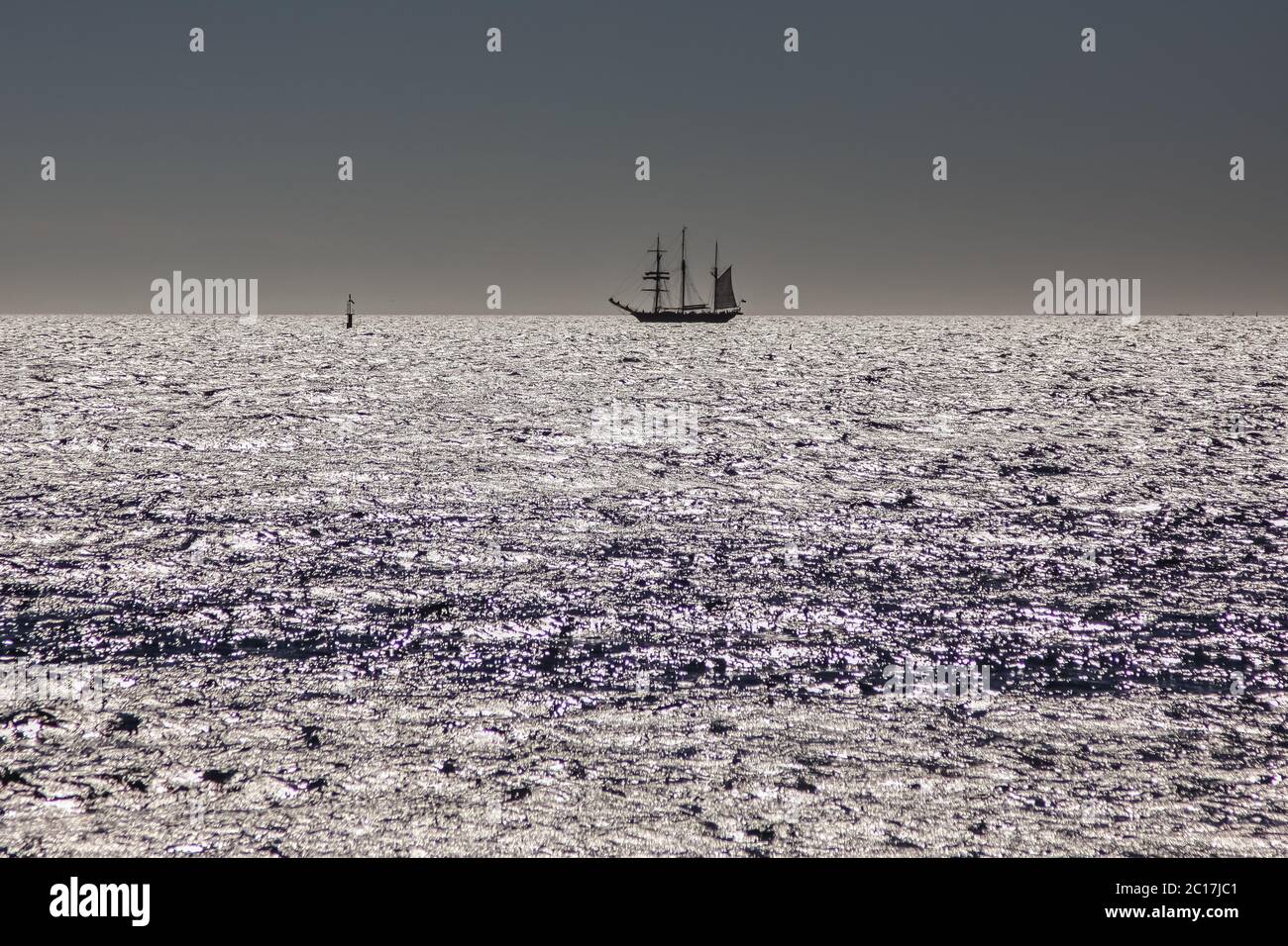View of the ocean with a sailing ship in the background reflecting sunset sky, Fremantle, Western Au Stock Photo