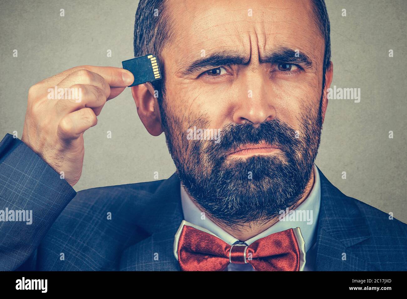 External memory needed concept. Portrait of interested bearded businessman wearing elegant jacket, red bow tie holding Micro SD card near head isolate Stock Photo
