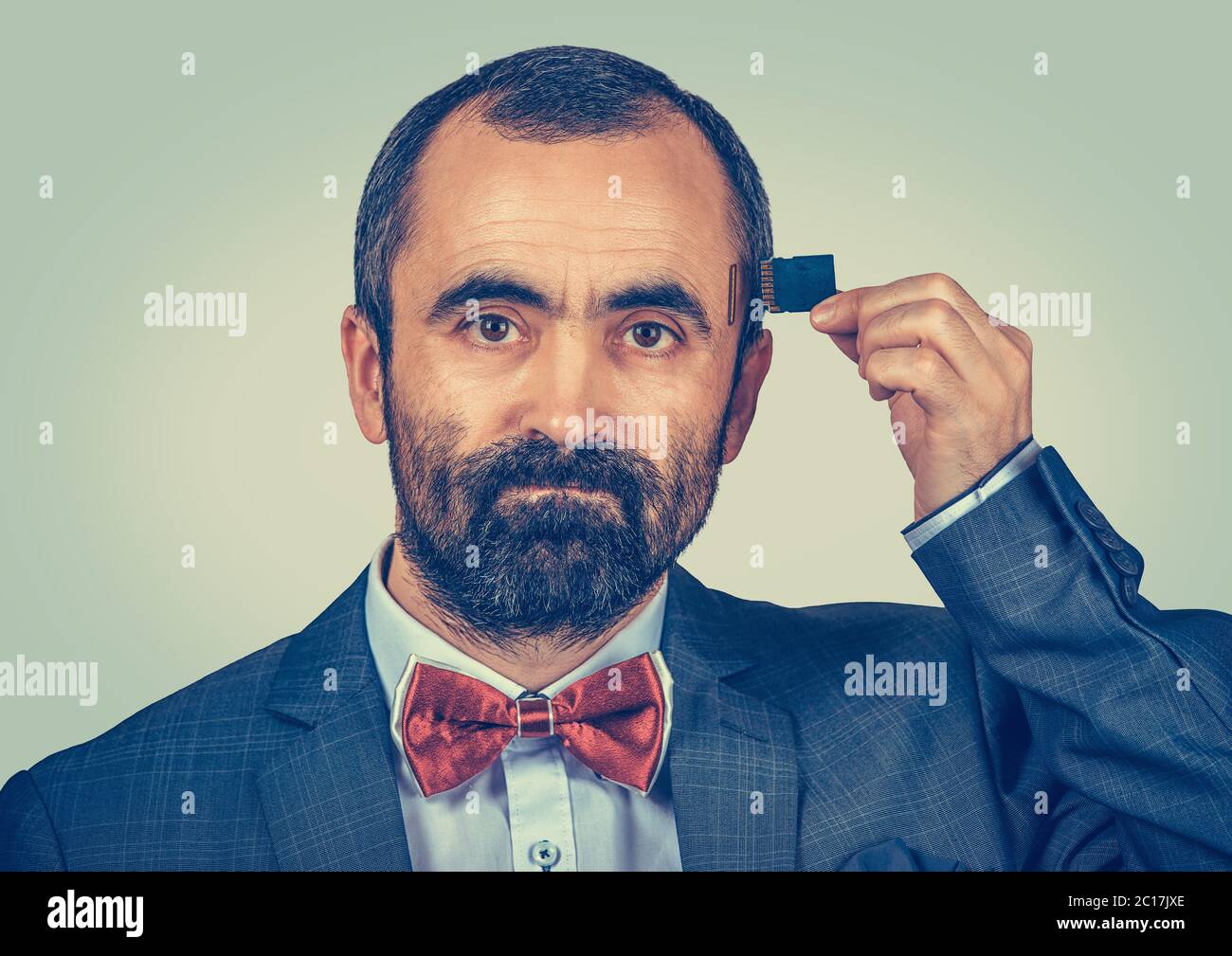External memory needed concept. Portrait of unhappy bearded businessman wearing elegant jacket and red bow tie holding Micro SD card near his head iso Stock Photo