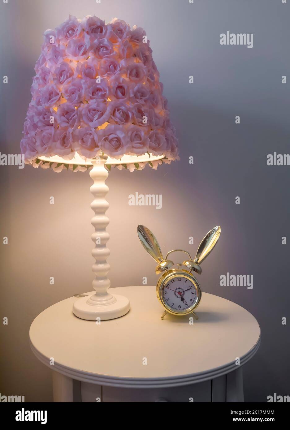 Lampshade with purple flowers beside an alarm clock on top of round side table Stock Photo