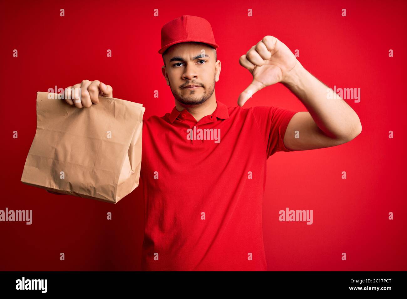 Young handsome delivery man holding paper bag with takeaway food over ...