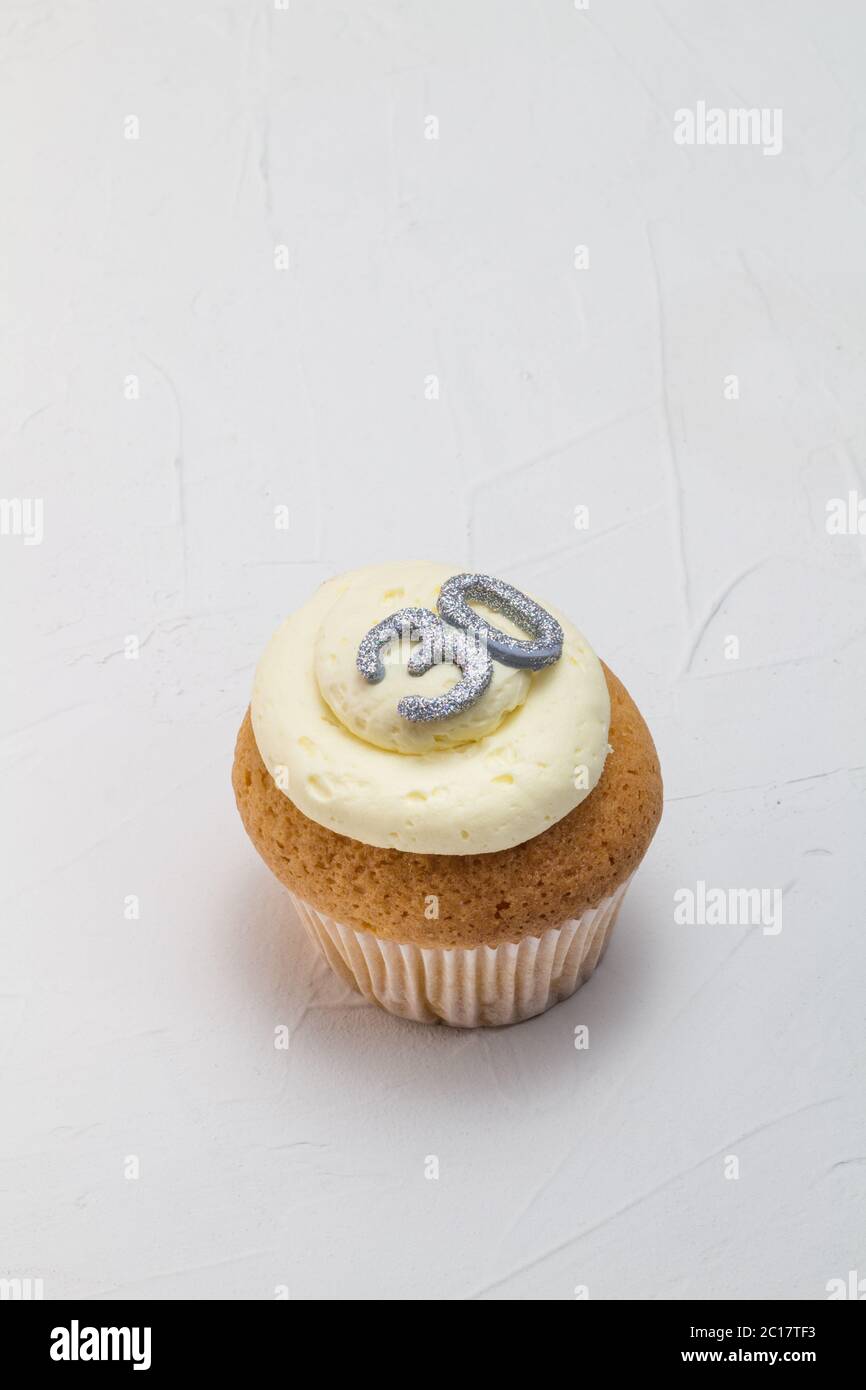 Single vanilla sponge cup cake with silver glitter number 30 on top of creamy white frosting Stock Photo