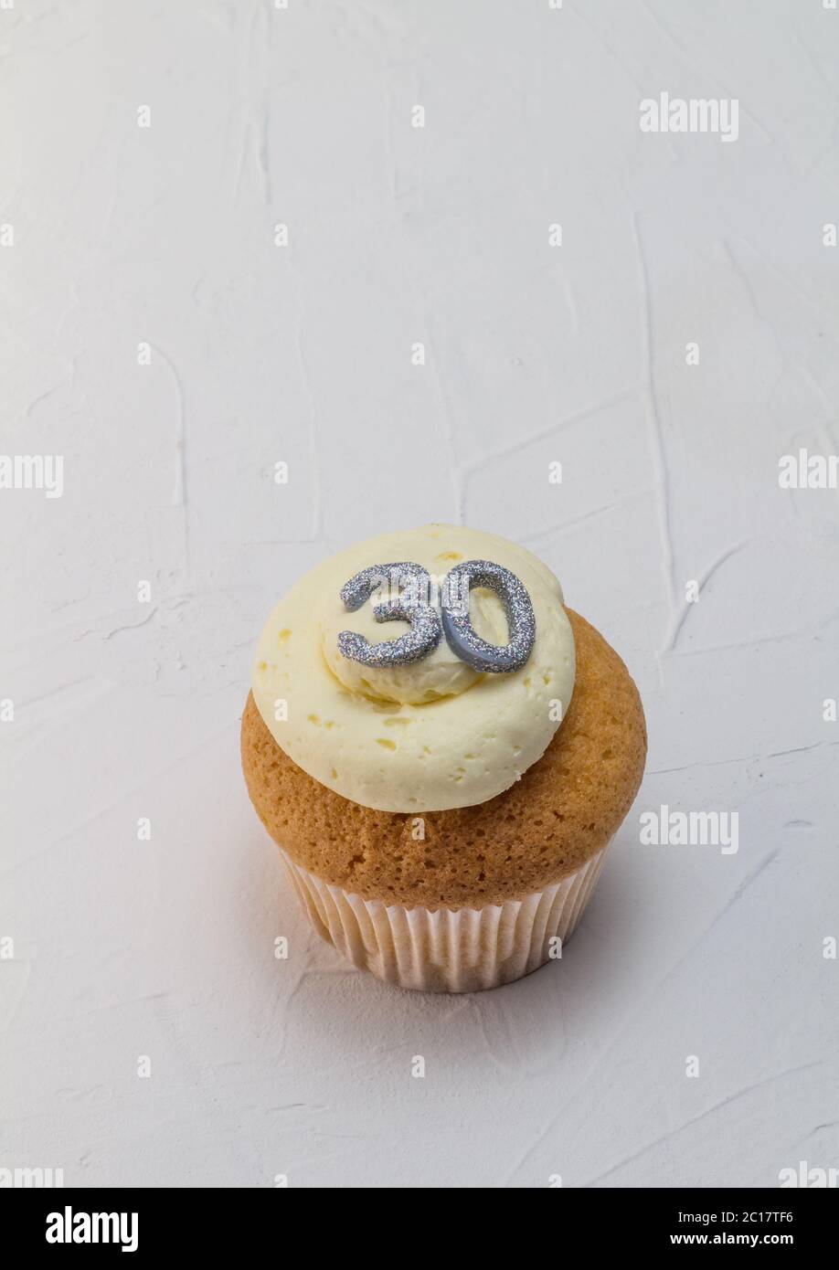 Single vanilla sponge cup cake with silver glitter number 30 on top of creamy white frosting isolate Stock Photo