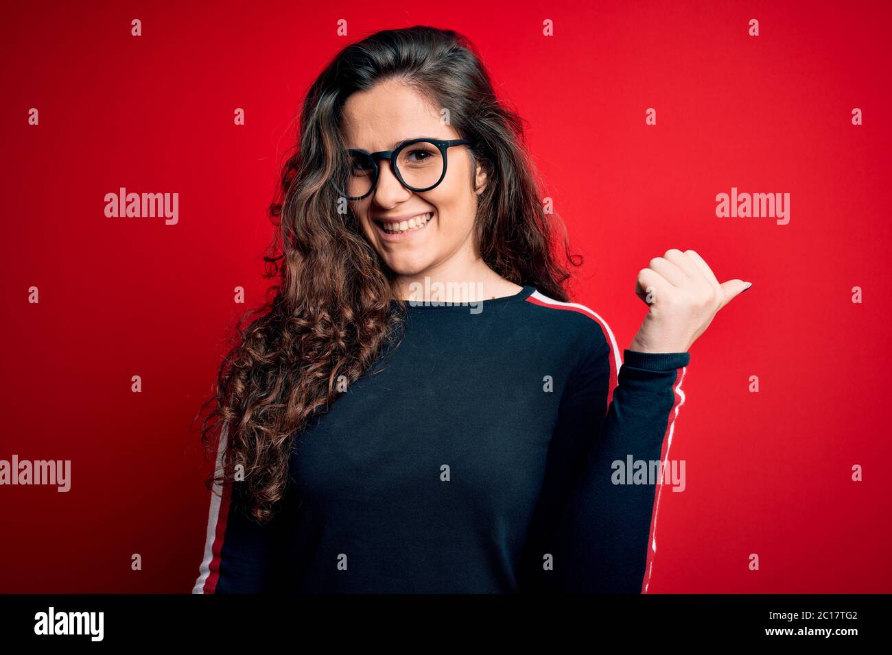 Young beautiful woman with curly hair wearing sweater and glasses over ...
