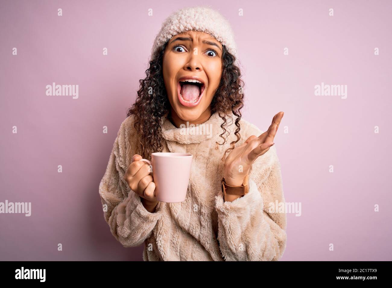 Young beautiful woman with curly hair drinking mug of coffee over isolated pink background very