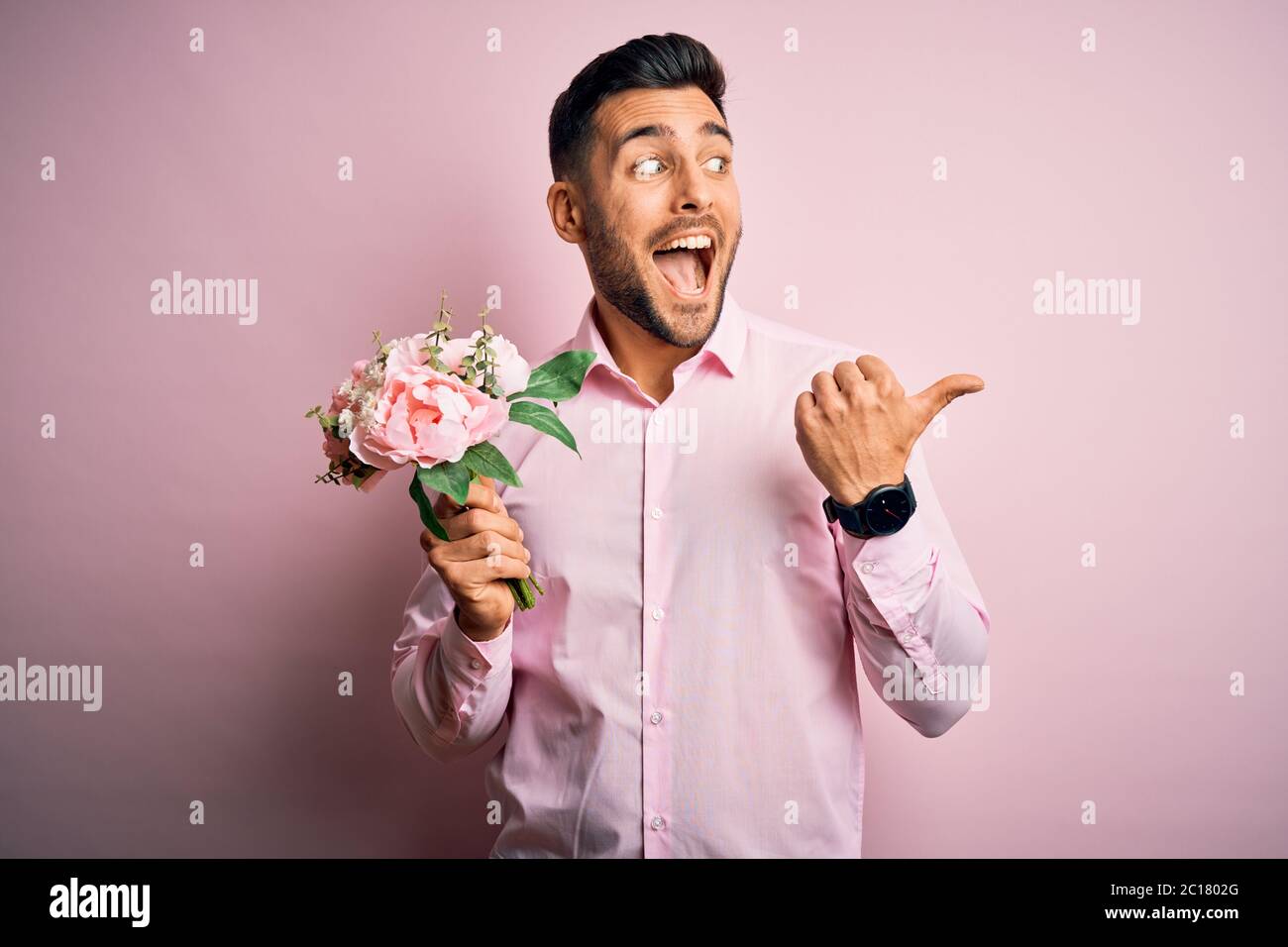 Young romatic man holding bouquet of spring flowers over pink isolatd ...