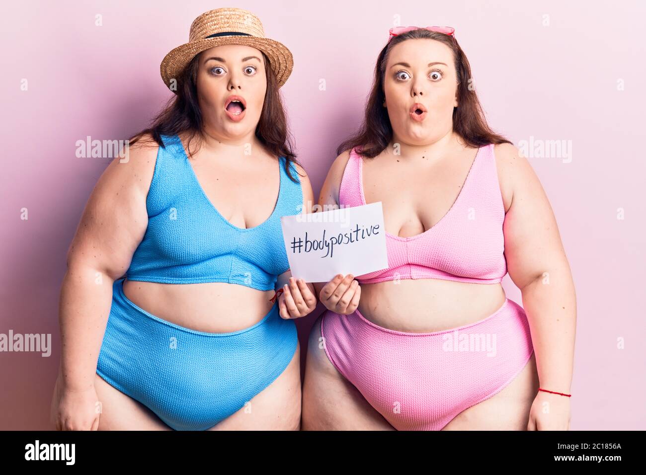 Young plus size twins wearing bikini holding paper with hashtag body  positive scared and amazed with open mouth for surprise, disbelief face  Stock Photo - Alamy