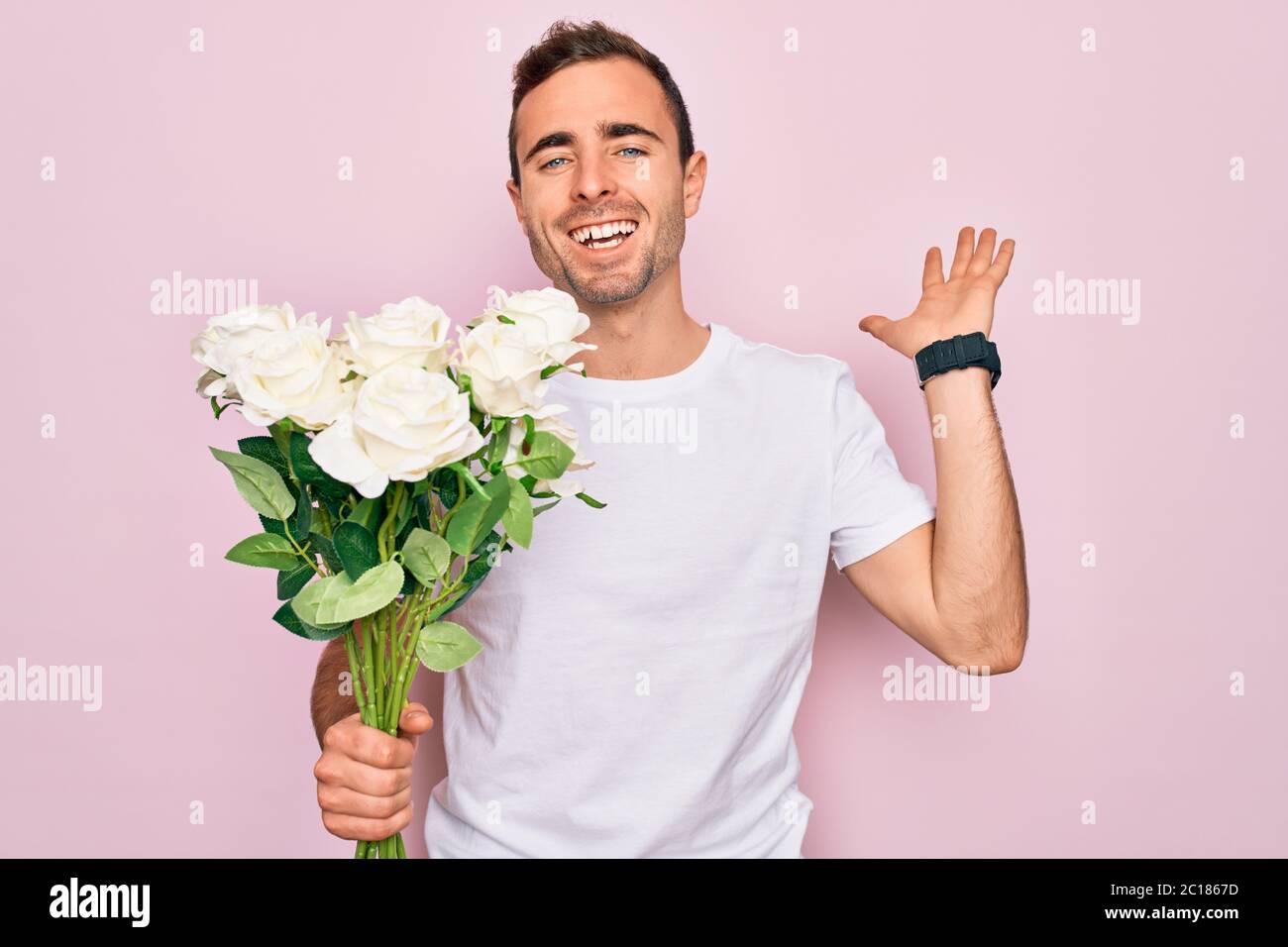 Young handsome man with blue eyes holding bouquet of flowers over pink ...