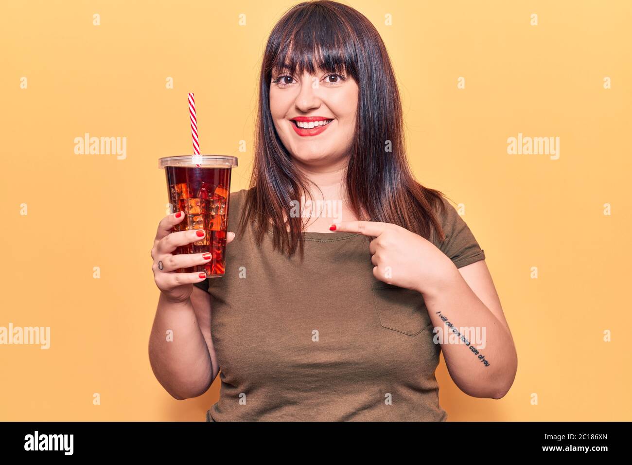 Young plus size woman drinking glass of cola beverage smiling happy pointing with hand and finger Stock Photo