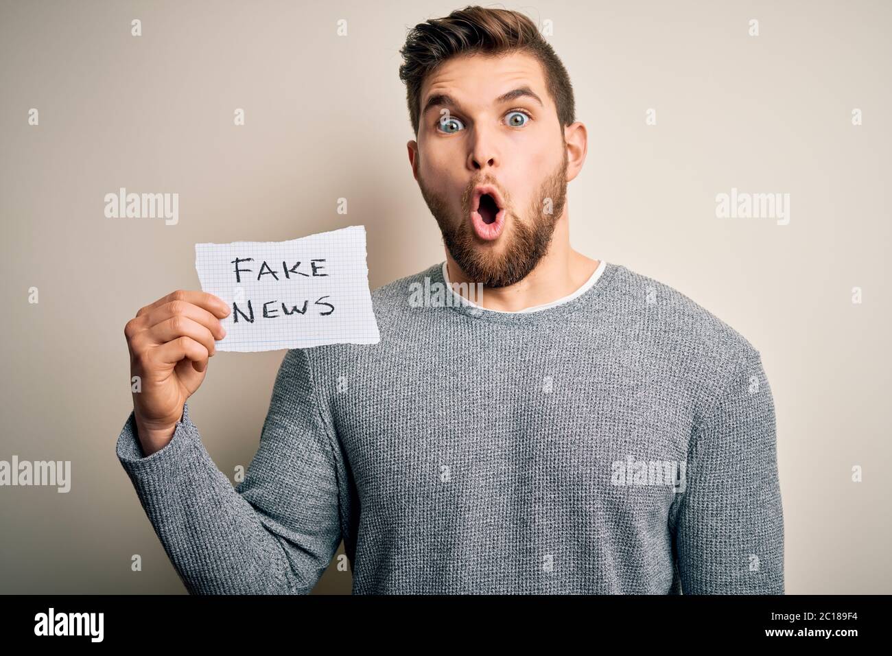 Young blond man with beard and blue eyes holding paper with fake news ...