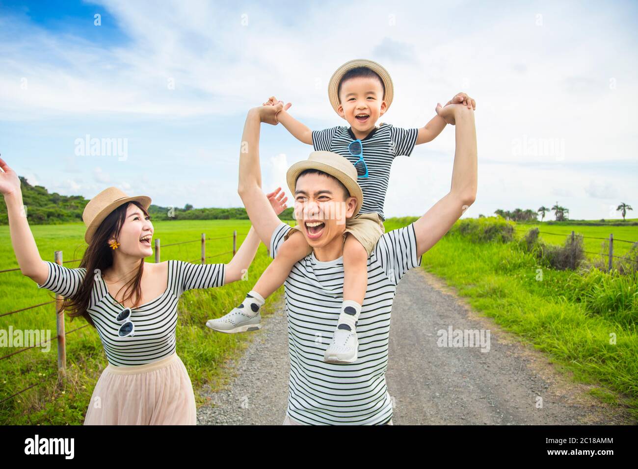 happy father giving son piggyback ride on his shoulders and walking on country road Stock Photo