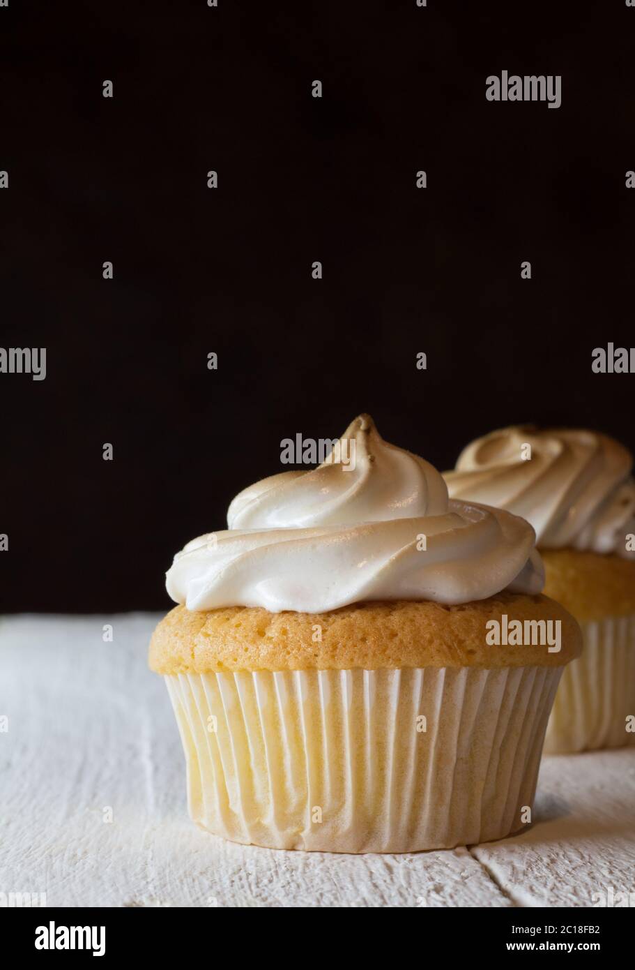 Cup cake with egg white meringue topping on white wooden table and one defocused against a dark bacg Stock Photo