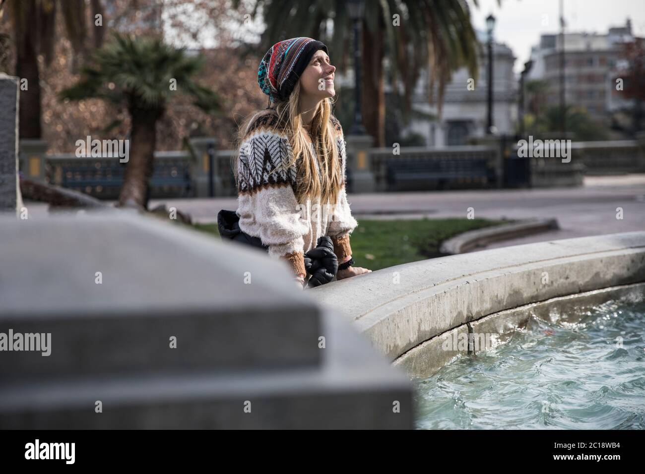 beautiful young blond woman near a water fountain looking up smiling Stock Photo