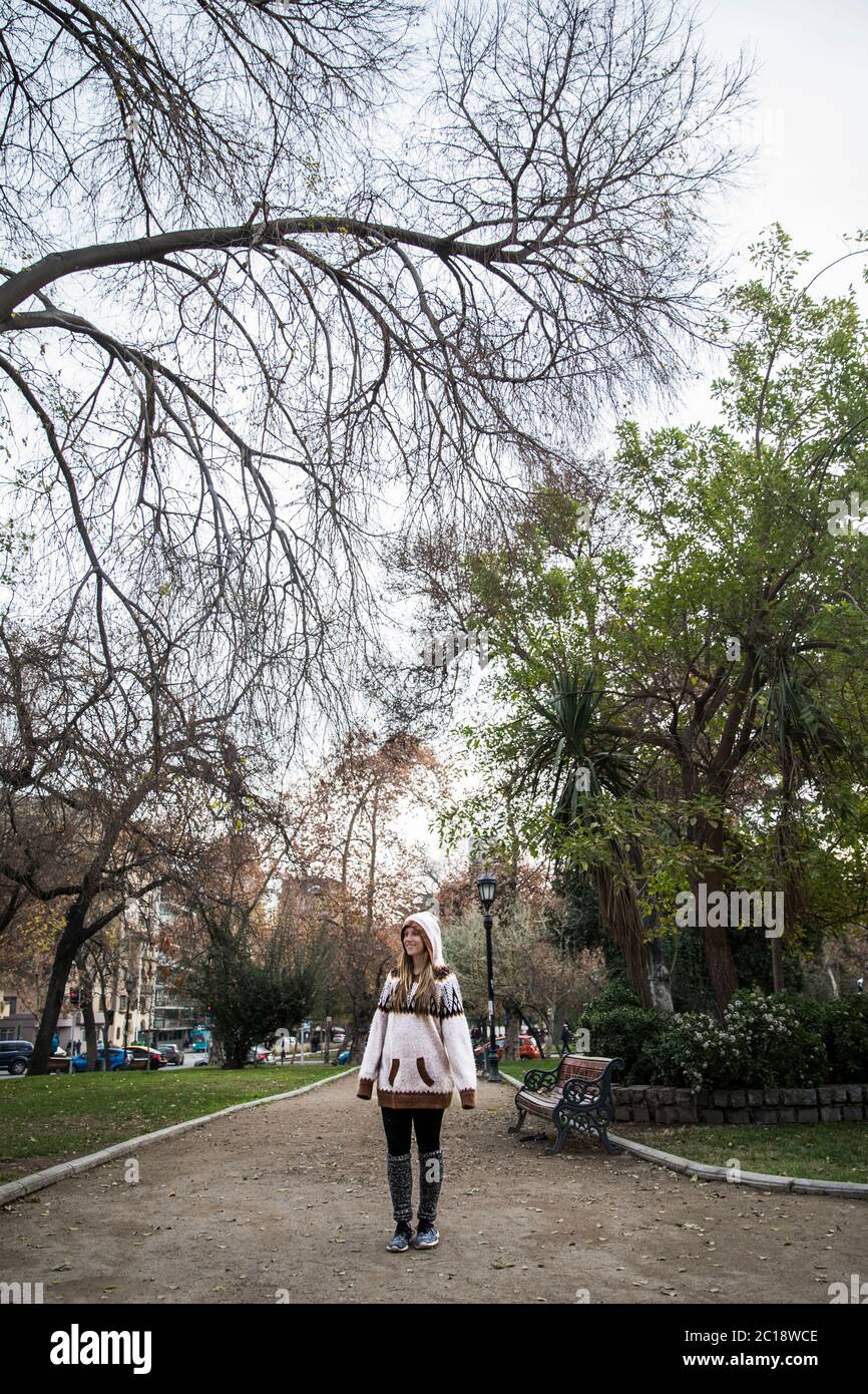 beautiful young blond woman standing in the middle of a park surrounded by trees Stock Photo