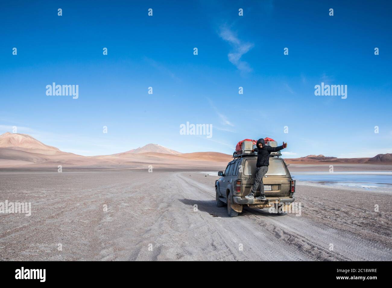 young, brown man standing on the back of an suv in the desert of bolivia Stock Photo