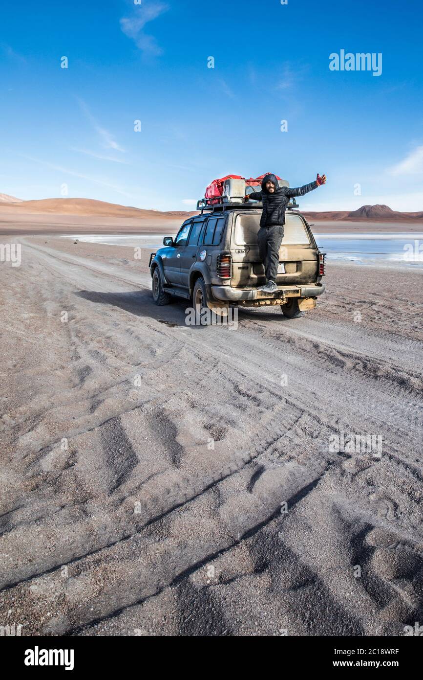 young, brown man standing on the back of an suv in the desert of bolivia Stock Photo