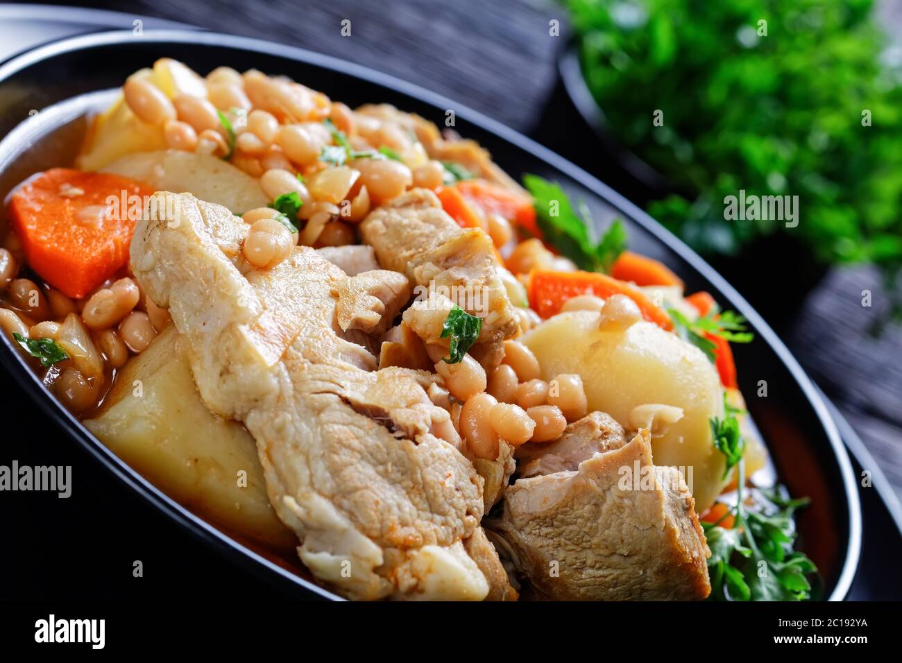 close-up of a portion of white bean, vegetables and pork steak stew in a black bowl on a dark wooden table, landscape view Stock Photo