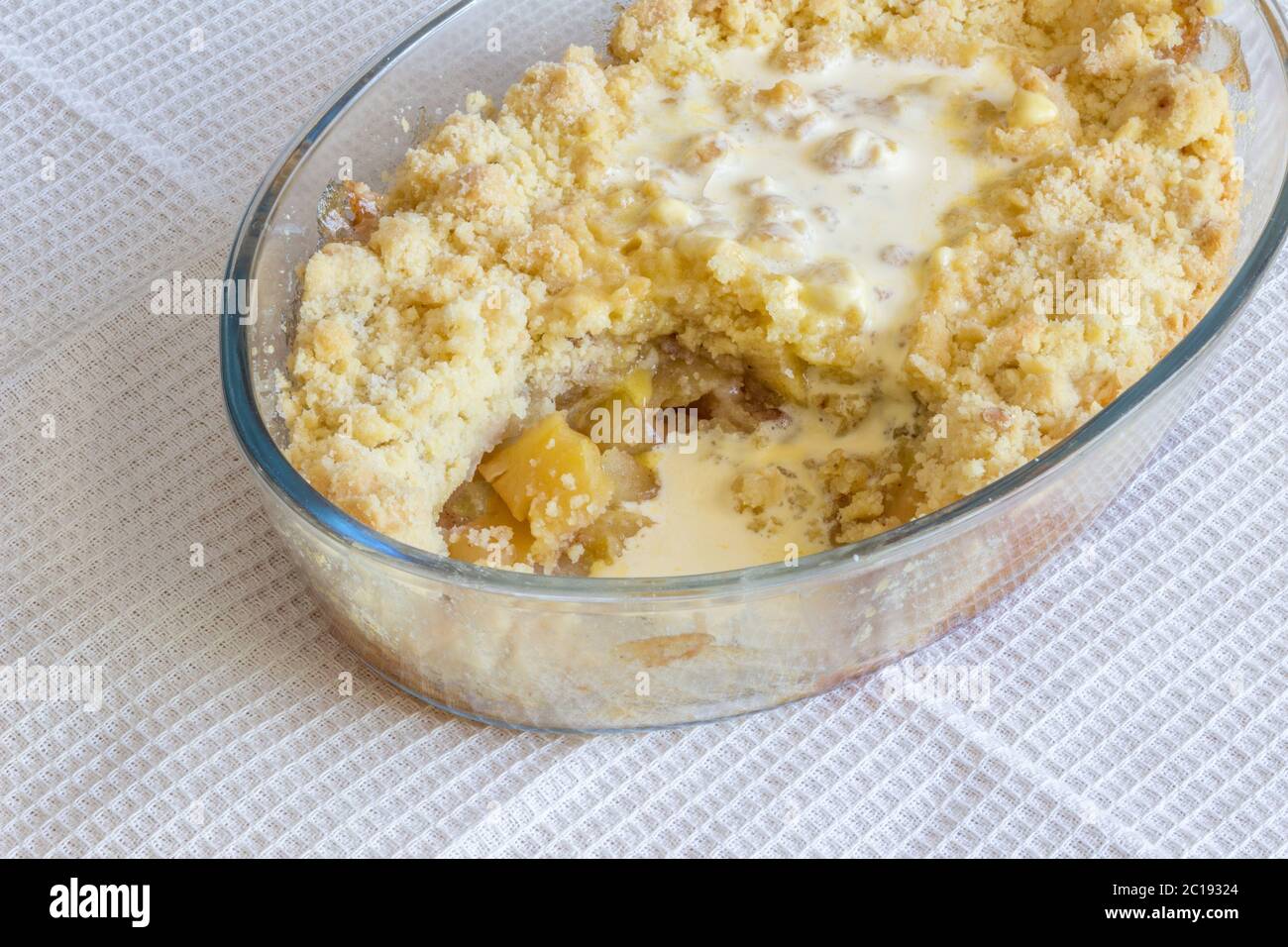 Cooked apple crumble pie in glass oval dish on white cloth Stock Photo