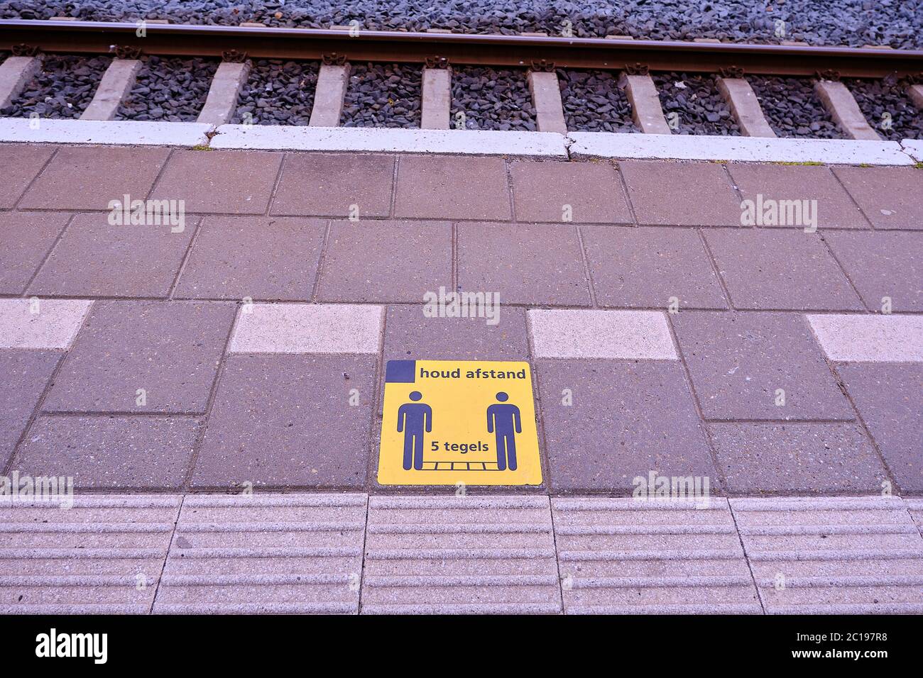 Yellow footprint sign on tiles in platform Dalfsen railway station. Dutch social distance words keep five tiles, 1,5 metres distance, against spread c Stock Photo