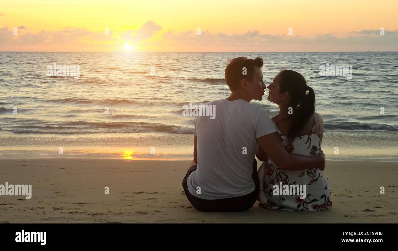 lovely young couple hugs and kisses sitting on empty ocean beach