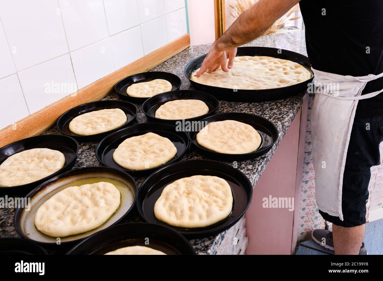 Chef stretching portions of pizza dough in individual baking trays in a pizzeria kitchen during preparation Stock Photo