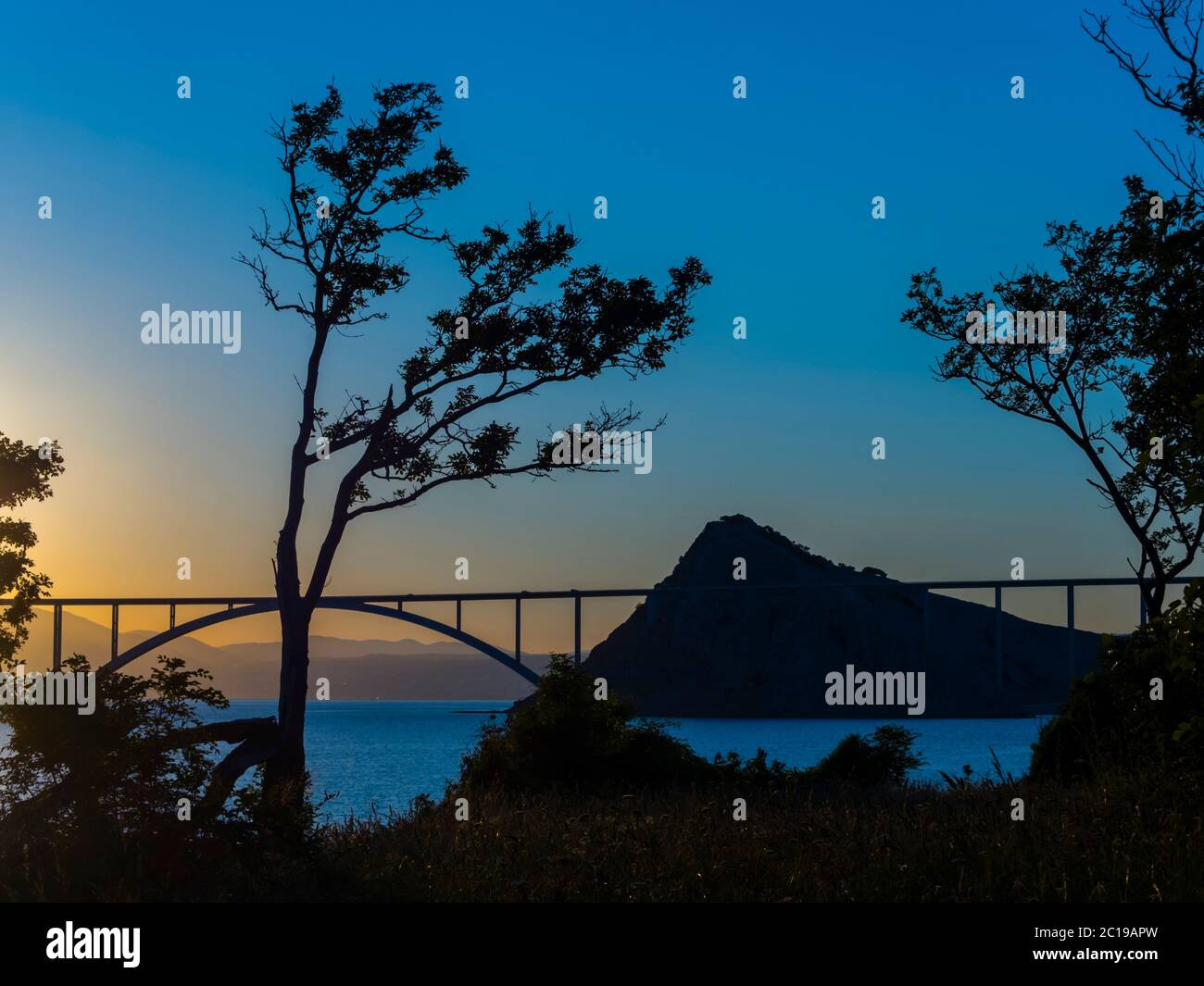 Sunset landscape silhouette silhouetting trees bridge mainland to island Krk Croatia Stock Photo