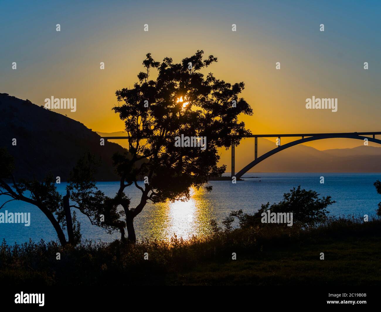 Sunset landscape bridge mainland to island Krk Croatia see view through dominant tree Stock Photo