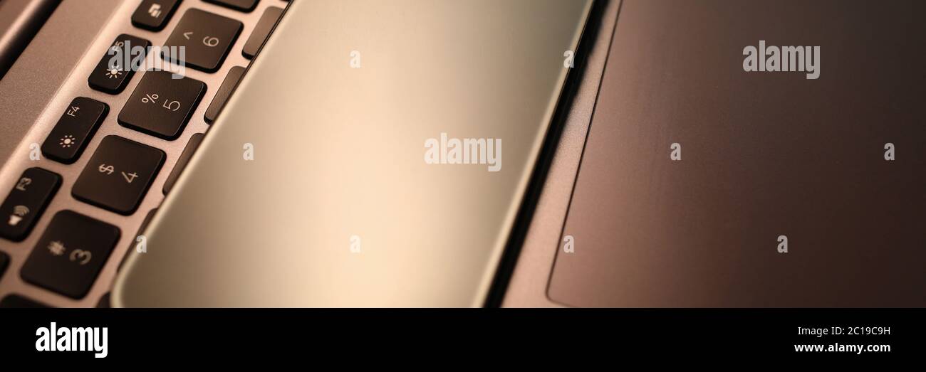 Silver smartphone lie on laptop keyboard in office close-up Stock Photo