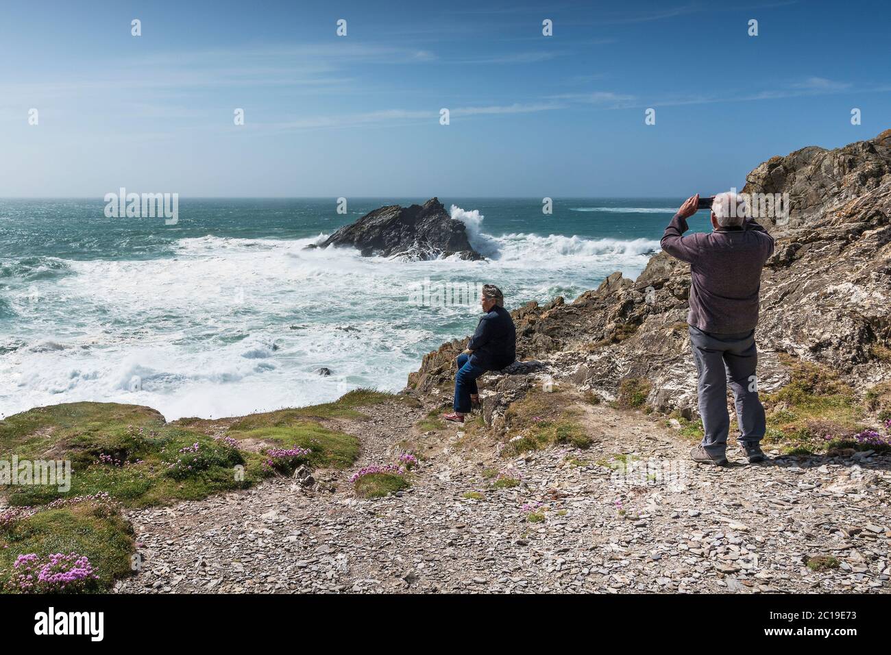 Tourists enjoying the wild windy weather and using a smartphone to photograph waves breaking over Goose Rock off the coast of Pentire Point East in Ne Stock Photo
