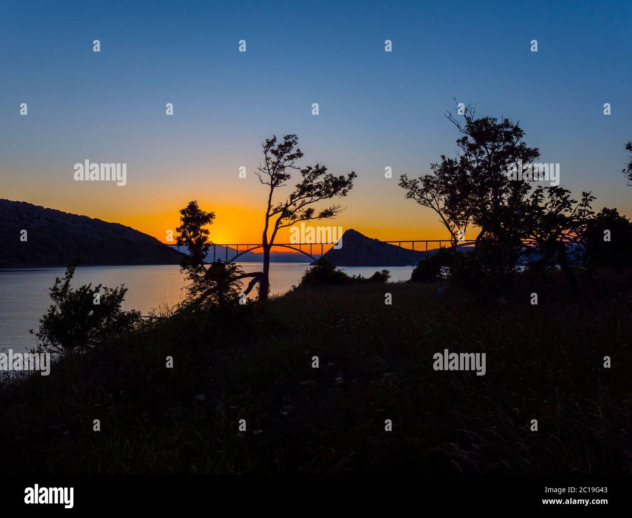 Sunset landscape silhouette silhouetting trees bridge mainland to island Krk Croatia Stock Photo
