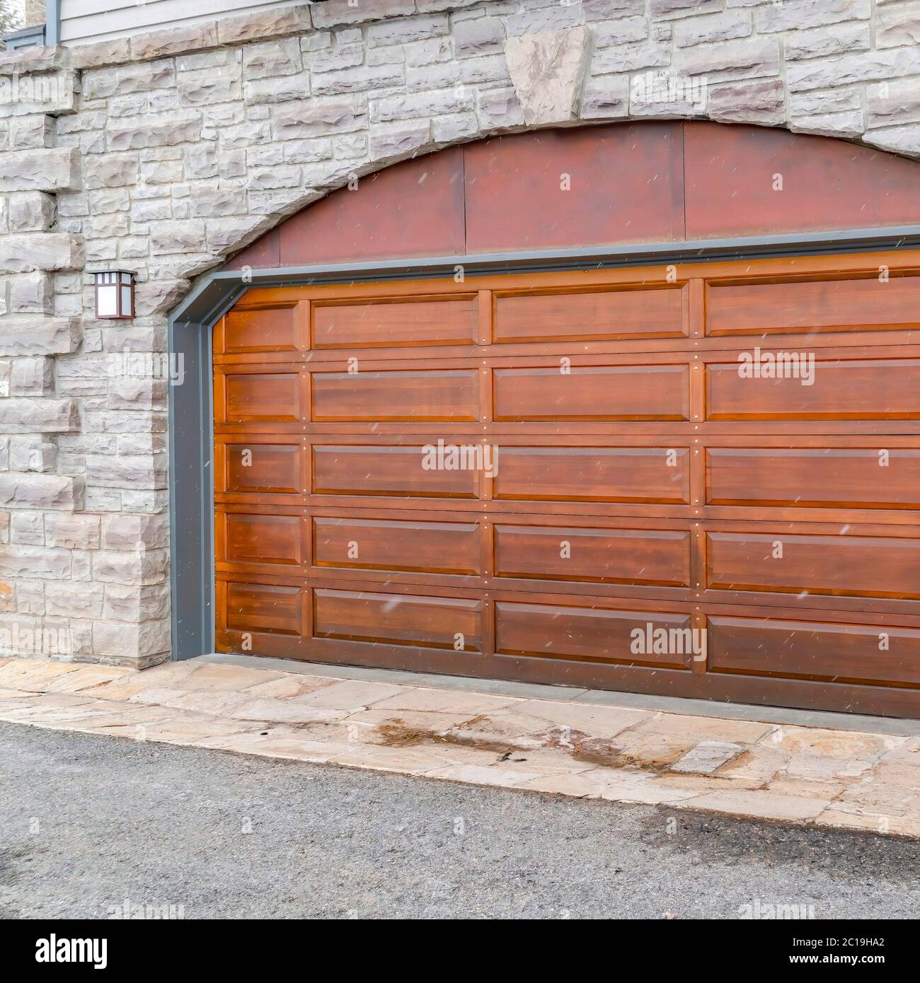 Square Arched brown wood panel garage door of home with stone brick