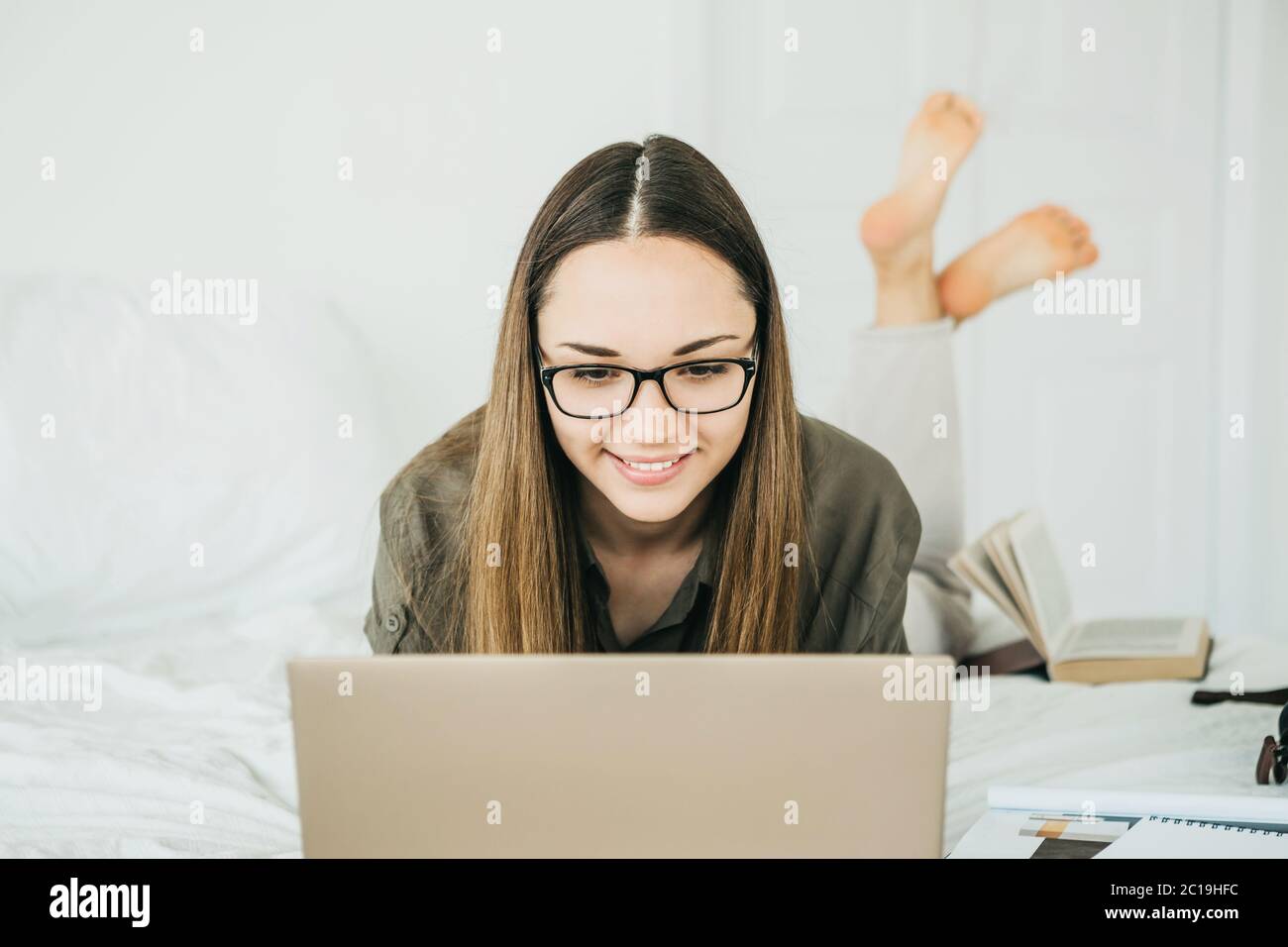 Beautiful smiling positive girl is using a laptop at home while lying ...