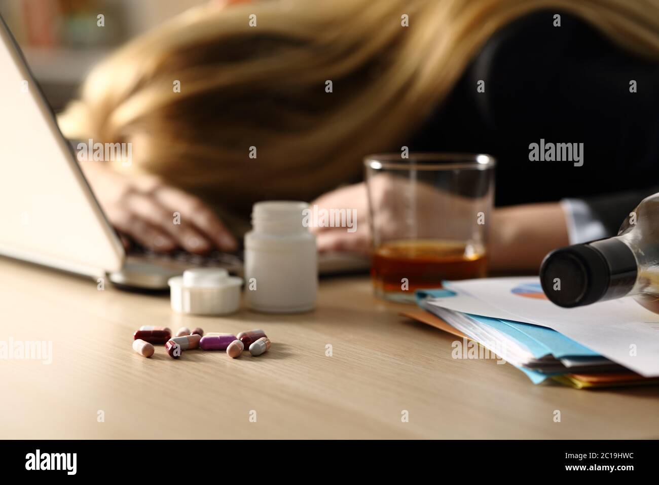 Close up of entrepreneur woman attempting suicide with pills and alcohol lying over desk at home office Stock Photo